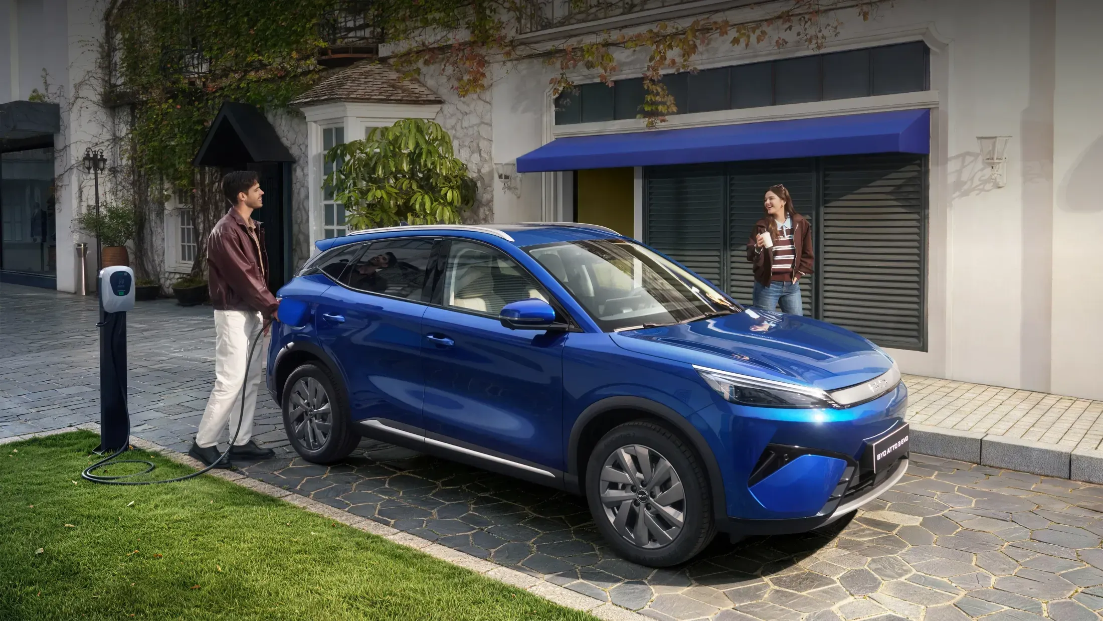 Paar lädt einen blauen BYD Atto 3 EVO an der Wallbox vor dem Haus