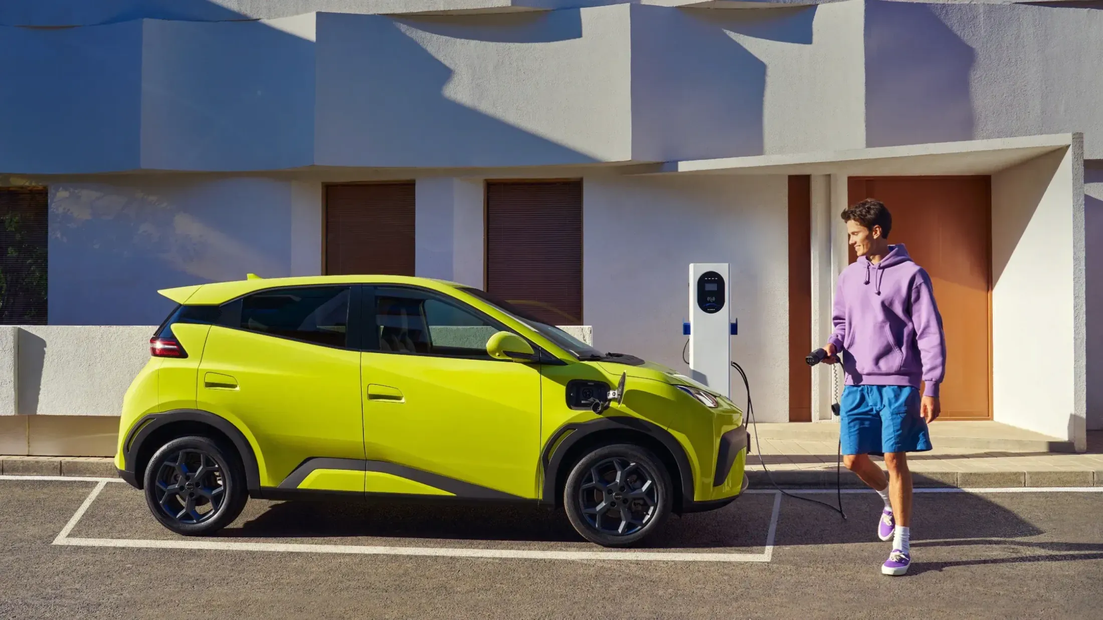 Junger Mann lädt den BYD Dolphin Surf an einer Wallbox vor dem Haus